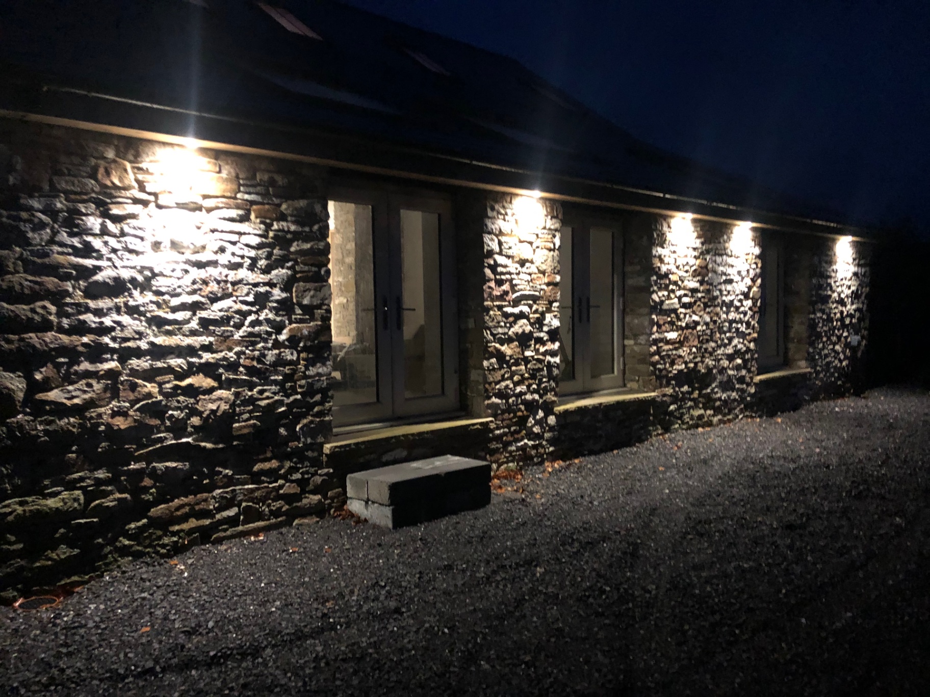 Stone barn exterior with wall-mounted uplighters at night